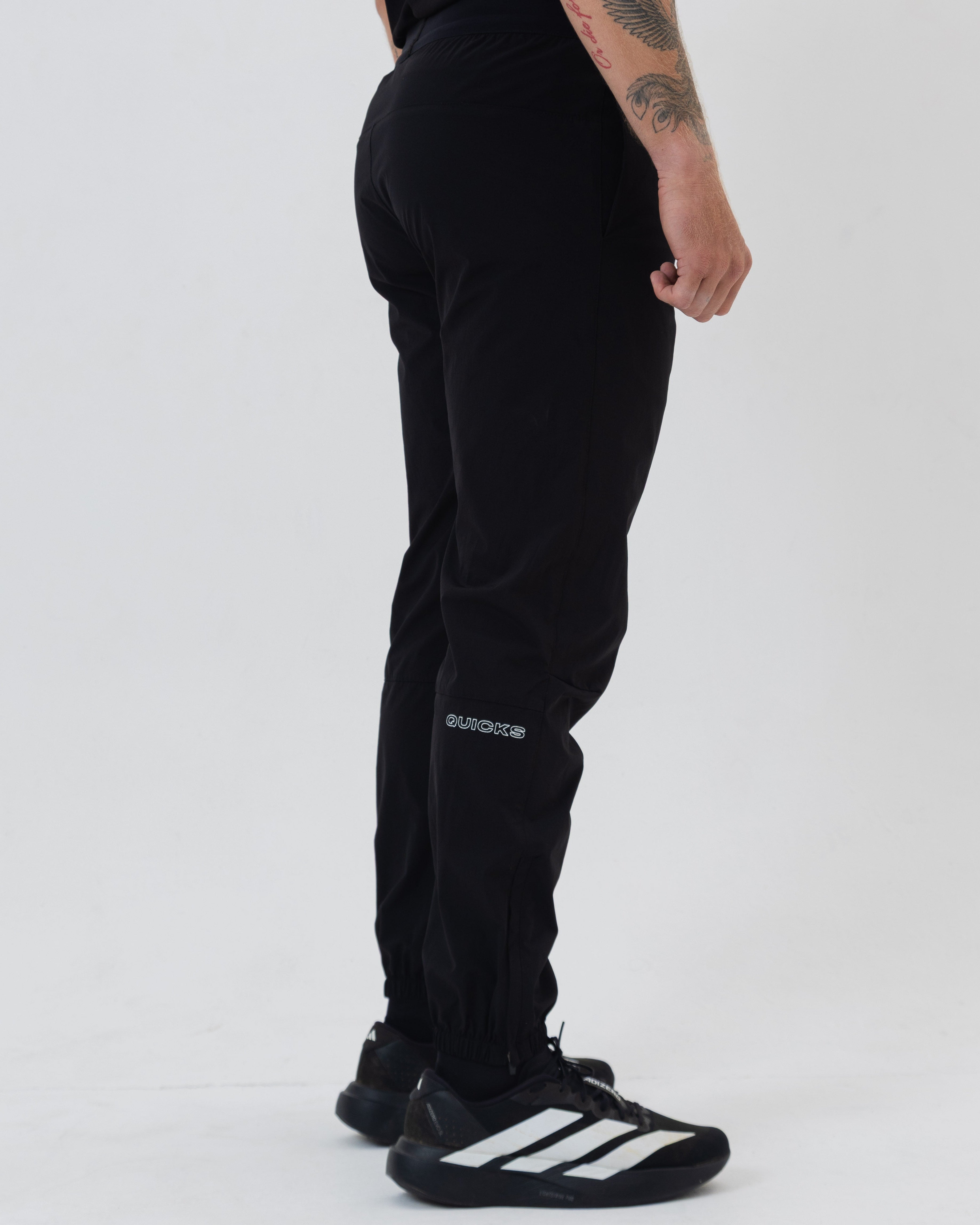 Person wearing black tracksuit pants with visible branding on a white background